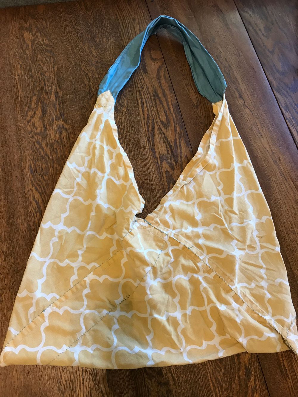 A yellow and white cloth shoulder bag with a teal shoulder strap on an oak table