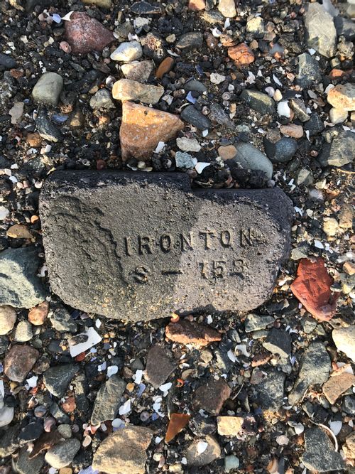 A dark grey worn cobble of some kind of old concrete or soft stone. Clearly a piece off some larger thing; it has the cut-off phrase "IRONTON" on one line, and below it "8-152".