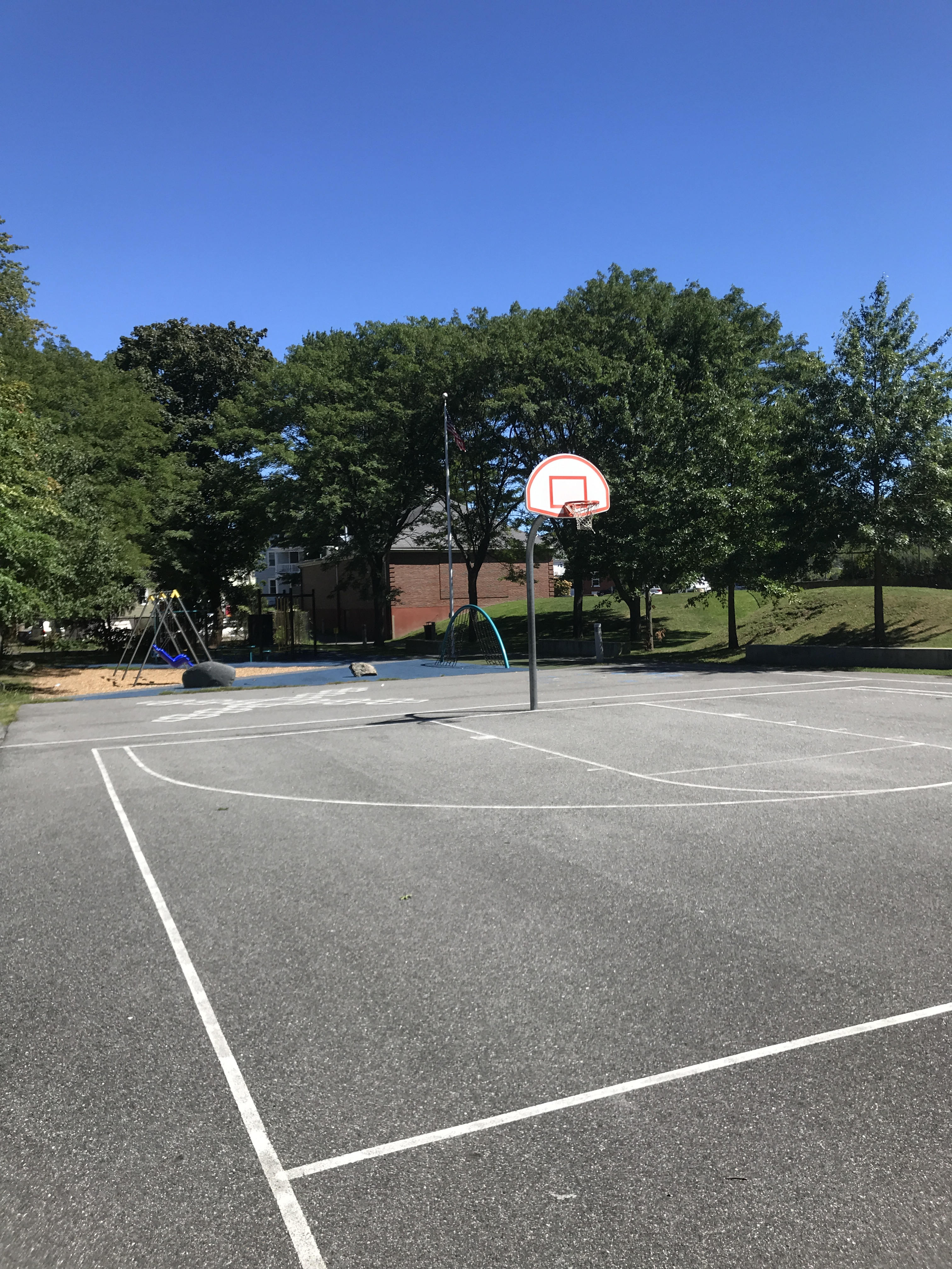 A view across a basketball court, with playground equipment in the background.