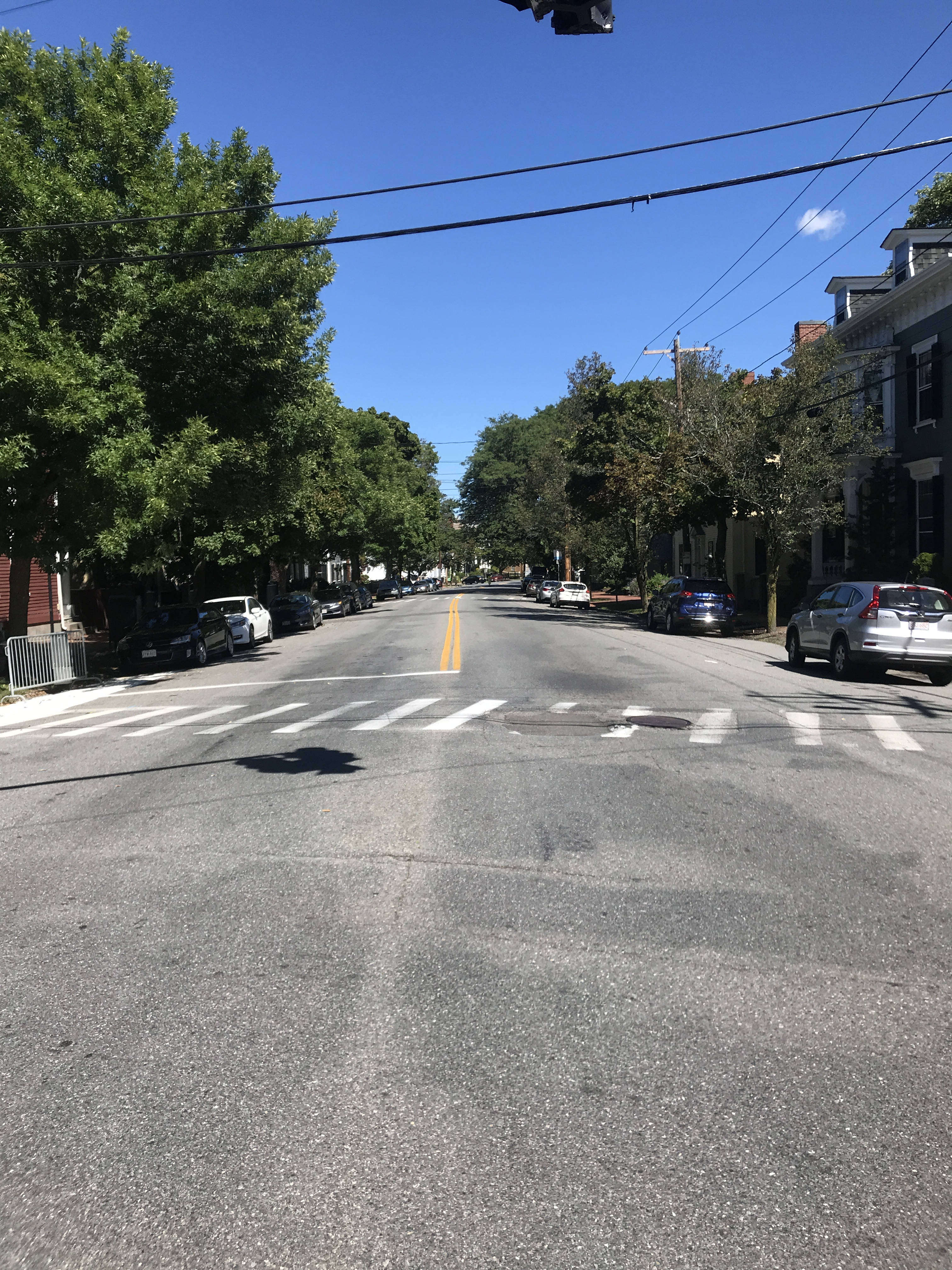 View down the center of Essex Street from Flint Street, looking downtown. Both sides of the street are lined with trees and cars. The street is wide.