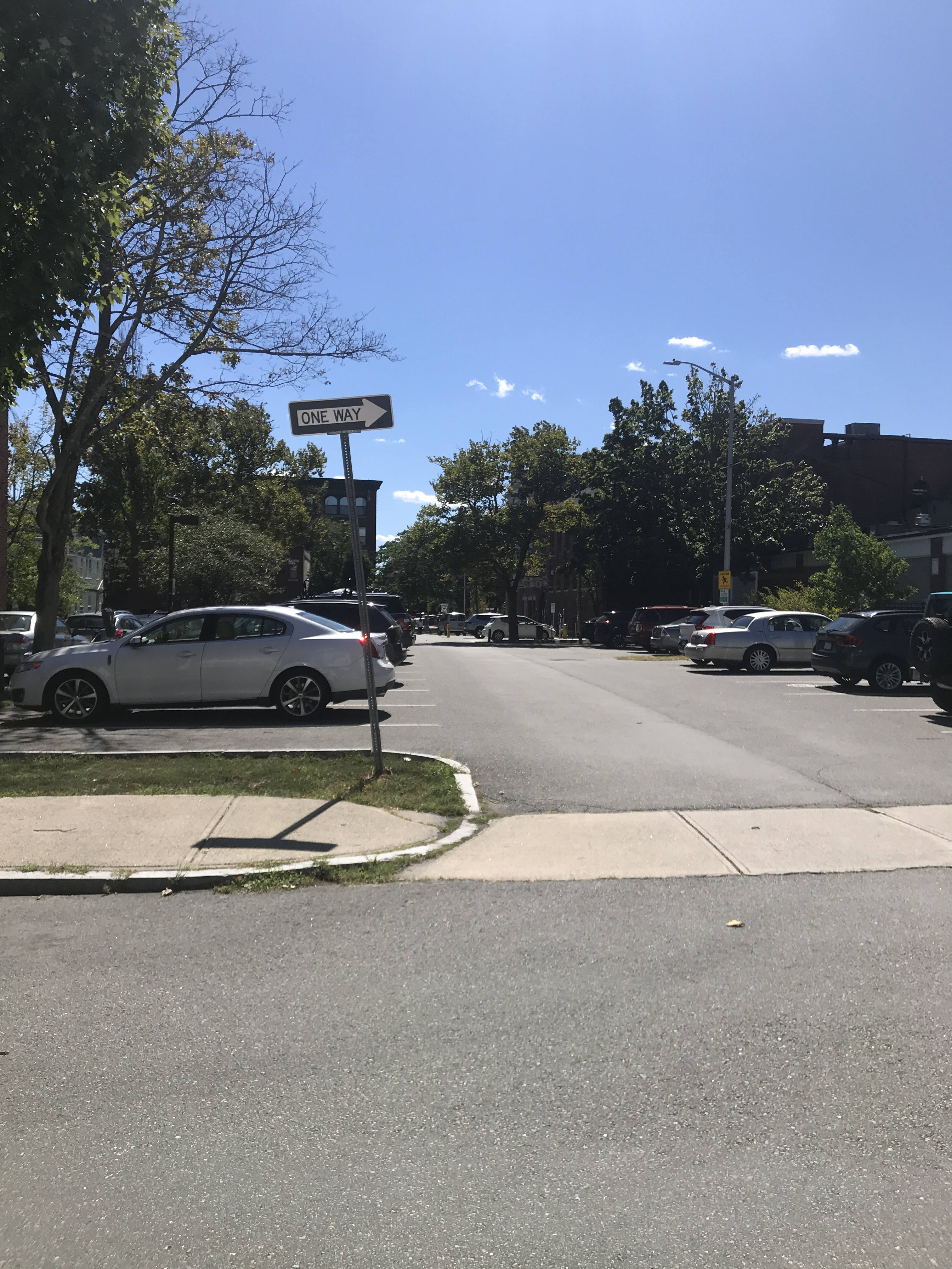 A view from one side of a street, across the street, where a parking lot also serves as a cross-street to the next street over